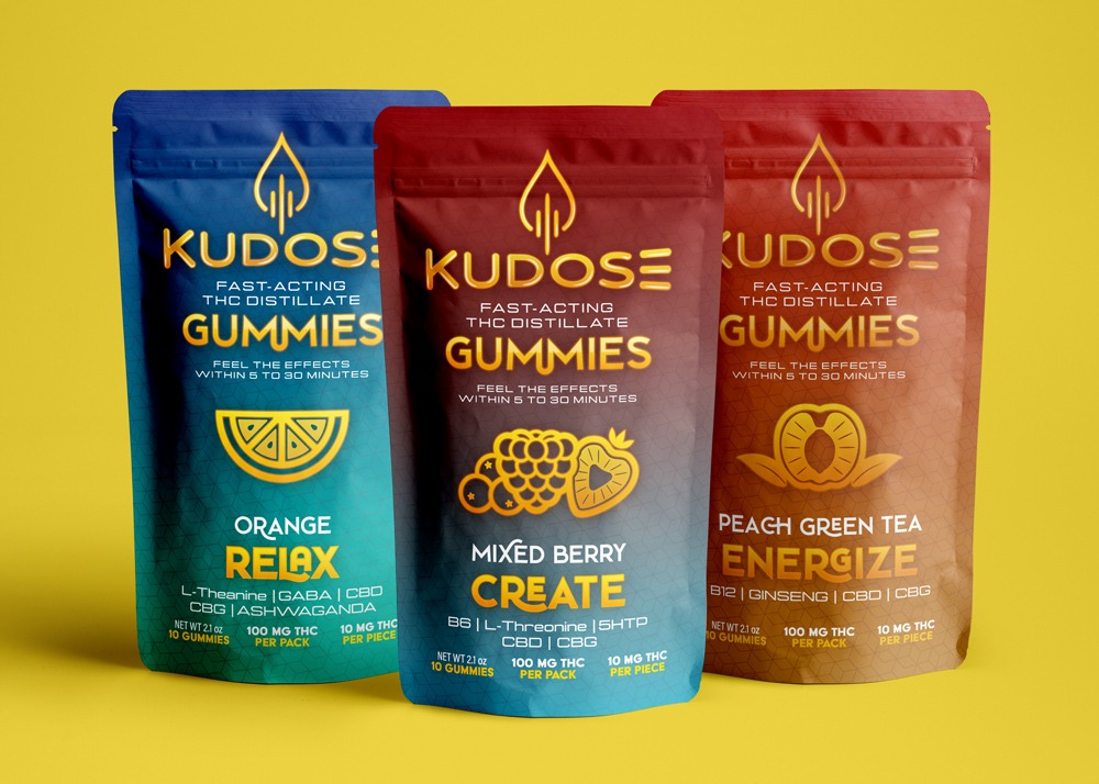 Photograph of three pouches of THC gummies on a yellow background. Each pouch says "Kudose Fast-Acting THC Gummies" Three flavors are present - Relax, Create, and Energize