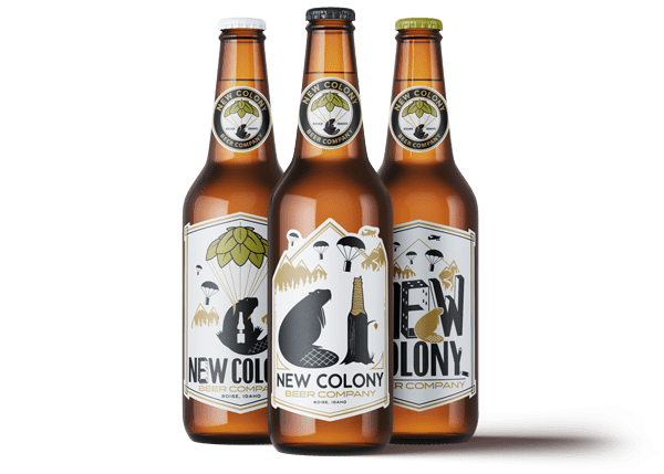 Three bottles of beer in a group. The label on the left most beer features a parachuting beaver holding a bottle of beer. The middle label features a beaver and a tree stump carved into a bottle of beer. The right most label is a beaver stepping away from a parachute while a plane flies overhead. Each has the text "New Colony Beer Company".